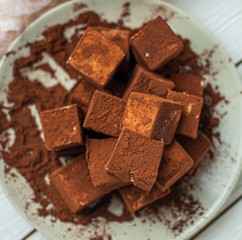 handmade souffle cubes covered with cocoa powder and pieces of chocolate lie on a plate on a light wooden table.