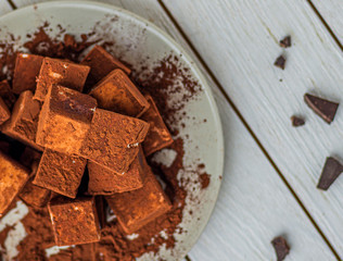 handmade souffle cubes covered with cocoa powder and pieces of chocolate lie on a plate on a light wooden table.