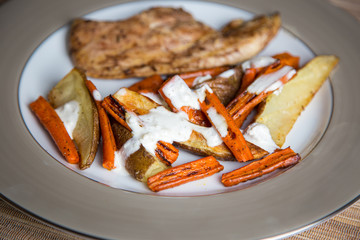 A simple, inexpensive meal: grilled chicken, roasted carrots and potatoes with a garlic sour cream...