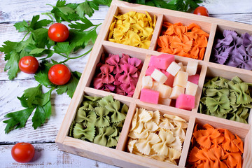 Multicolored pasta farfalle and cubes of cheese in wooden box
