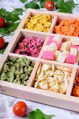 Multicolored pasta farfalle and cubes of cheese in wooden box