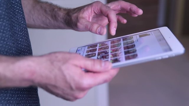 The movement of male hands. A man flips through the pages of a tablet with his fingers. A man views photos on the iPad.