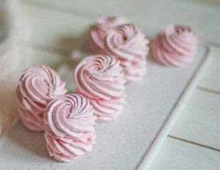 pink marshmallow zephyr lies on a white plate on a wooden table. Top view close up