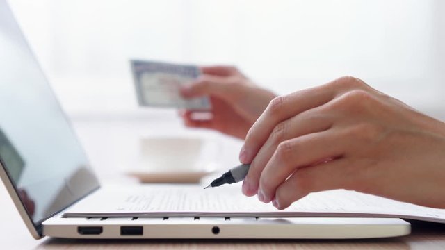 Woman freelancer with paper documents work on laptop at home-office. Blurred female hand hold social security number on background. Businesswoman fill out tax return form at work. Dolly shot