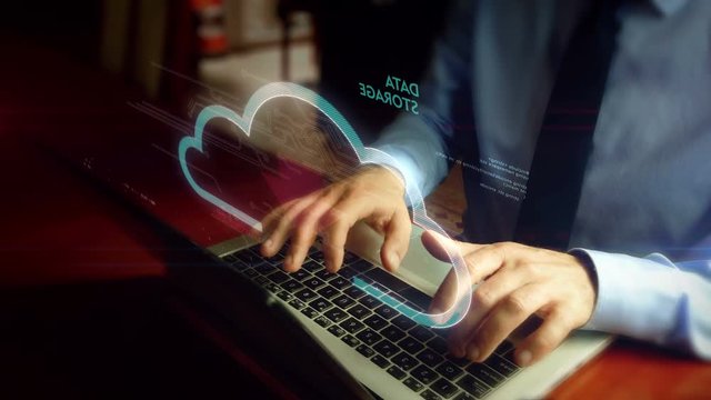 Man typing on laptop with data cloud hologram screen over keyboard. Data computing, online storage and document archive concept. Natural hand camera shake.