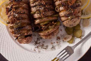 Baked potato with onions and spices on a white dish on the background of a wooden table