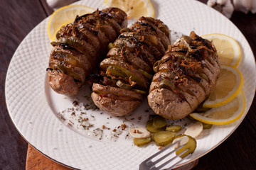 Baked potato with onions and spices on a white dish on the background of a wooden table