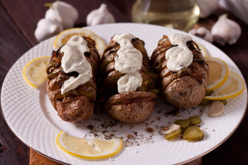Baked potato with onions and spices on a white dish on the background of a wooden table