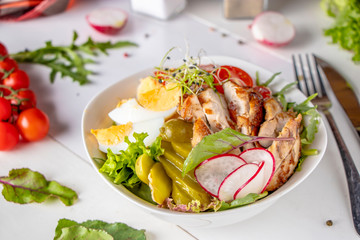 Healthy Buddha bowl lunch with baked chicken, quinoa, cherry tomatoes, radishes, eggs, pickles...