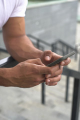  Male strong muscled  hands holding black smartphone and typing message leaning on stair linen. closeup front view photography. Background of stadium stairs blurred. 