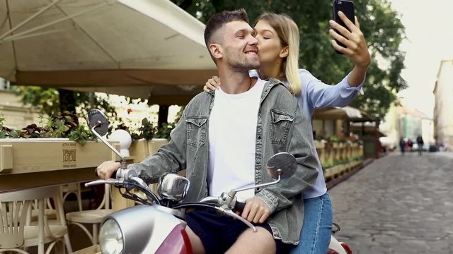 Happy couple on scooter making selfie photo on smartphone outdoors. People Travel On Weekend. High Resolution.