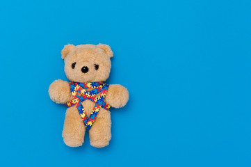 World Autism Awareness day, mental health care concept with teddy bear and ribbon puzzle pattern. On blue background.