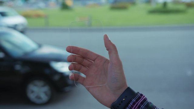 Augmented reality and future concept. Young man using transparent mobile phone with innovative touchscreen for animation. In background cars driving backwards. Time effects.