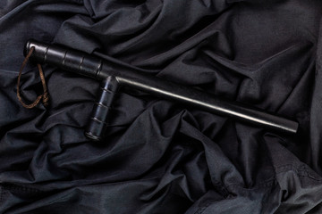 black rubber police baton on black shirt wrinkled cloth low-key flat lay