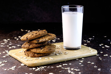  Homemade oatmeal cookies and glass of milk on dark rustic background.