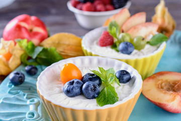 Delicious cream Panna Cotta dessert decorated with various berries, fruits and mint leaves in ceramic form on a wooden table next to ingredients, closeup