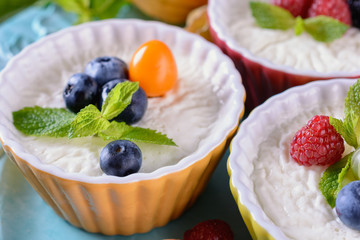 Delicious cream Panna Cotta dessert decorated with various berries, fruits and mint leaves in ceramic form on a wooden table next to ingredients, closeup