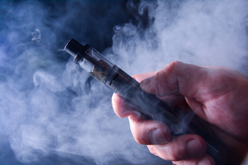 Abstract image of an electronic cigarette in a hand on a background of smoke. Copy space. The...