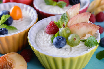 Delicious cream Panna Cotta dessert decorated with various berries, fruits and mint leaves in ceramic form on a wooden table next to ingredients, closeup