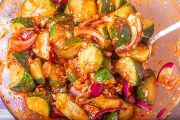 Oi Muchim Korean spicy cucumber salad in a glass bowl with spoon close-up, top view.