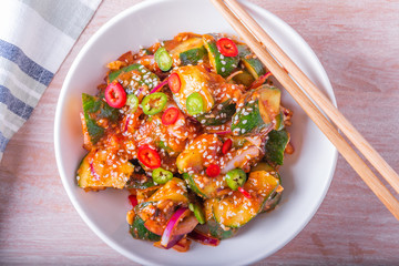 Oi Muchim Korean spicy cucumber salad with sesame seeds in a bowl and chopsticks on a wooden table, top view.