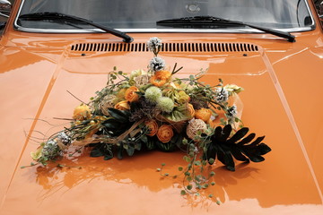 Dekorativer Hochzeitsstrauß in Orange auf der Motorhaube der schwedischen Limousine der...