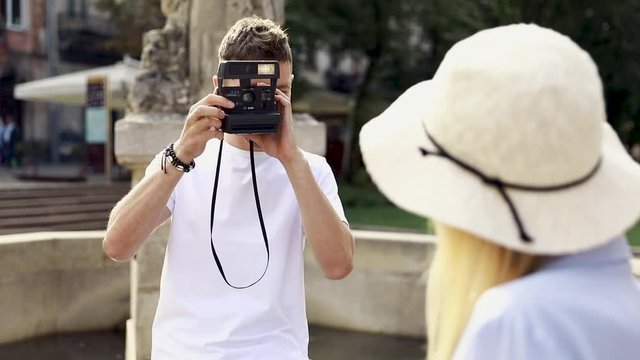 Tourist Couple. Man With Camera Taking Photos Of Woman In Street. Smiling Young Couple In Love In Stylish Clothes Traveling And Making Photos Outdoors. People Travel On Weekend. High Resolution.