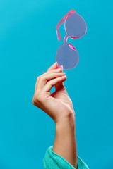 Photo of hand with pink sunglasses on empty blue background