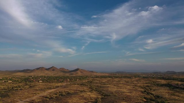 Drone footage rising up over the Sonoran Desert of Arizona during a sunset with partly cloudy skies and a desert community in the foreground
