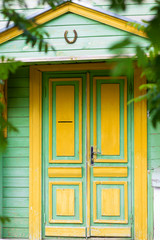 Beautifull green and yellow wooden door with horse shoe over it. Russian style. Architecture. Hand made carving, pattern Vertical