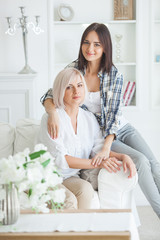 Fototapeta na wymiar Mature mother and her adult daughter together. Women indoors portrait. Middle age woman and her daughter at home sitting on the couch.