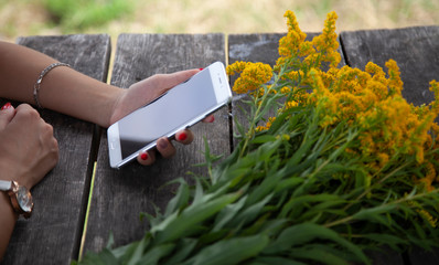 in the girl’s hand is a phone, a blank screen for text, flowers are on the table