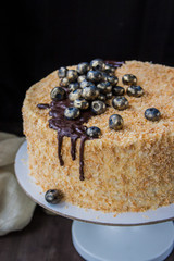 A close up of a homebaked Napoleon cake decorated with guilt blueberries and ganache, set on the pedestal cake plate against black background