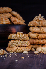 Homemade peanut cookies in stacks in front of a dark handmade peice of pottery full of cookies against black background