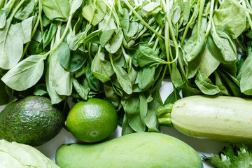 Fresh green vegetables variety on rustic white background from overhead, celery, avocado, cabbage, mango, cucumber, spinach, lime, squash. Healthy, vegetarian concept. Flat lay, top view