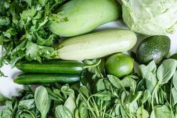 Fresh green vegetables variety on rustic white background from overhead, celery, avocado, cabbage, mango, cucumber, spinach, lime, squash. Healthy, vegetarian concept. Flat lay, top view