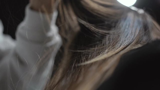 A male hairdresser divides light-brown hair and combs a lock of it