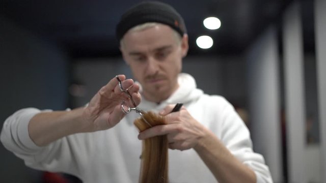 A middle plan of a male hairdresser milling a lock of a brown hair and combing it