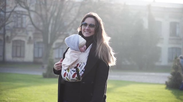 A young woman straighting her long hair and carrying her one year old daughter in a baby sling in front of a castle