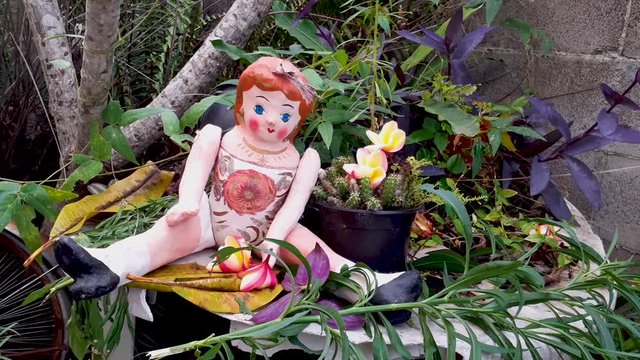 Traditional Mexican handmade doll, made of cardboard, redhead, sitting in garden with tree and flowers, by day