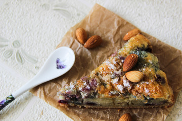 Close-up the slice of cake with berries and almonds decorated with powdered sugar and spoon on a craft napkin. Almonds lie next to the cut piece of cake. Homemade bakery cake. Breakfast dessert.
