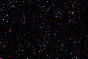 Drops of water in the air, against a black sky. Violet or purple tinted. Abstract or background image, selective focus.