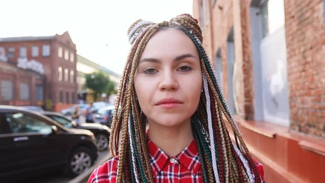 Portrait of smiling trendy teenage girl with dreadlocks in urban background, slow motion