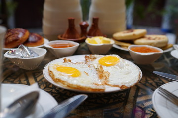 Fried eggs on the plate for breakfast. In the background is honey, jam, cheese, butter and pancakes.