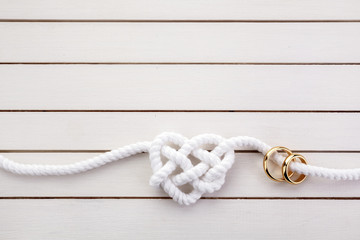 Heart shaped rope and a double gold ring on white wooden background