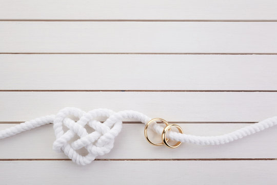 Heart shaped rope and a double gold ring on white wooden background