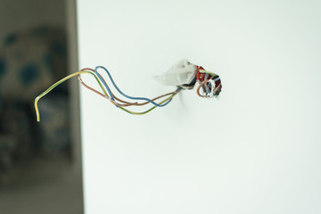 protruding wires from the outlet. Unfinished home repair on a white wall with whitewash. Open...