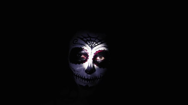 Halloween mask. A girl in a blinking and frightening light. Mexican day of the dead. Portrait of a young woman with scary makeup for Halloween on a dark background. 4K