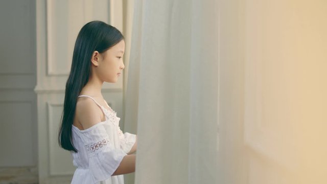 nine-year-old beautiful little asian girl with black long hair looking out of window