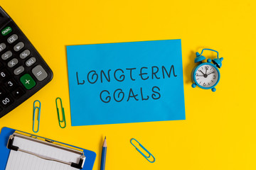 Handwriting text Longterm Goals. Conceptual photo Strategic target that is required more time for completion Clipboard sheet clips note calculator pencil alarm clock colored background